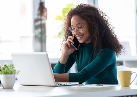 Woman smiling on her phone while working at a laptop