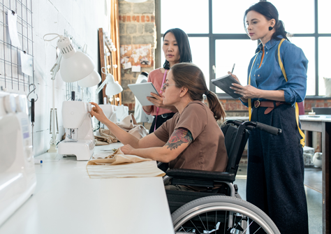 Three women working in a sunny fashion design office. One is in a wheelchair.