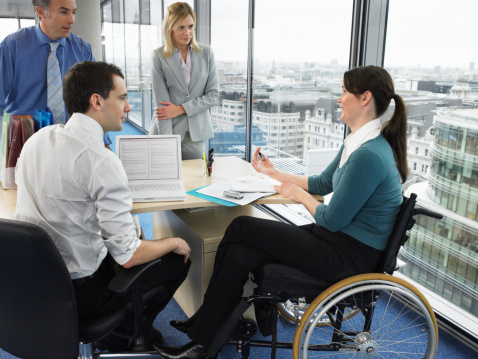 A team working at a table. a woman in a wheelchair is part of the group and they are listening to her speak.