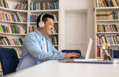 Man using a laptop with headphones and a screen reader in a library